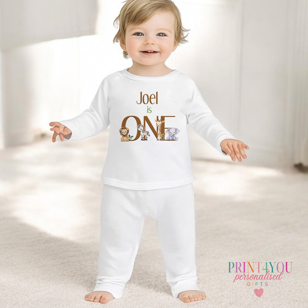 Personalised first birthday pyjamas in white cotton, printed with safari animals and a custom name and ONE, 6-12 months.