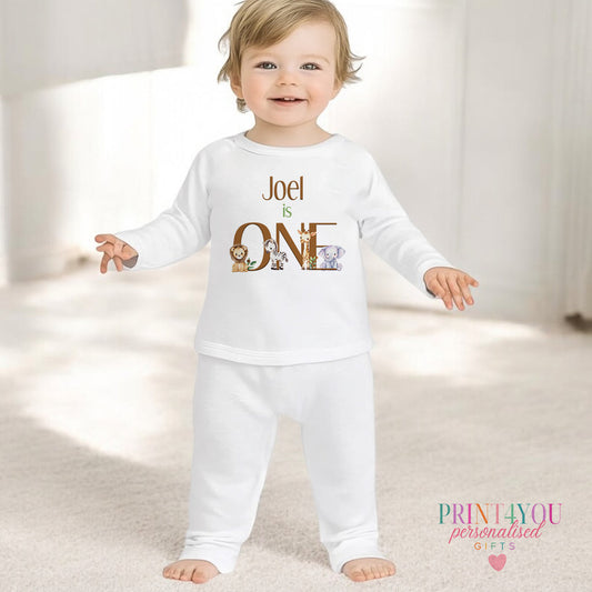 White cotton baby pyjamas with a safari animal design and personalised 'ONE' text, size 6-12 months.