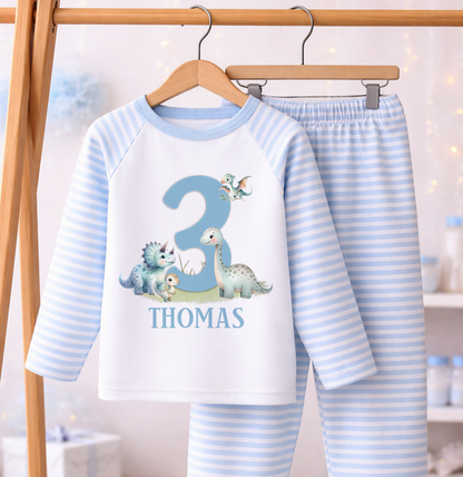 Blue and white striped pyjama set printed with a dinosaur design, personalised name and age, laid flat against a white background