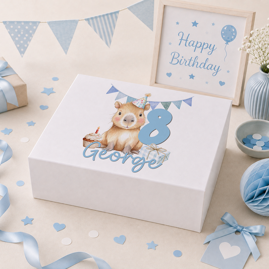 Personalised white keepsake box with magnetic lid, showing a party-hatted capybara beside a cupcake and a wrapped gift, a pastel blue number 8 and the name George, styled with birthday bunting, balloons and confetti props