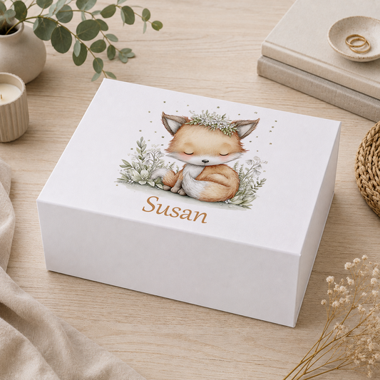 Personalised sage green baby fox keepsake box with magnetic lid, showing a sleeping baby fox curled among white flowers with the name Susan in script, on a wooden tabletop with eucalyptus and candles