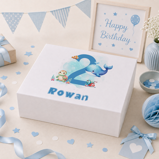 Blue personalised birthday keepsake box lid featuring a whale, sea turtle, clownfish and hermit crab swimming around a large number, with the child's name and age in ocean-blue script