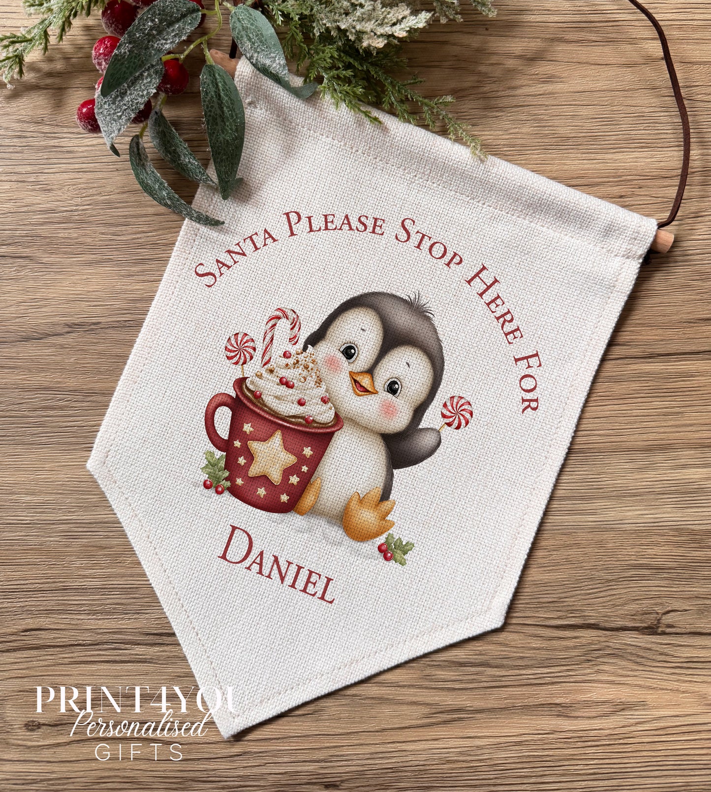 Personalised linen Christmas banner featuring a penguin holding hot chocolate beside a Santa Please Stop Here message, personalised with the name Poppy, hung on a wooden bar