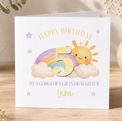Birthday card featuring a colourful illustration of a sun, clouds and a rainbow, printed with 'Happy Birthday to a Gorgeous Granddaughter Lara'.