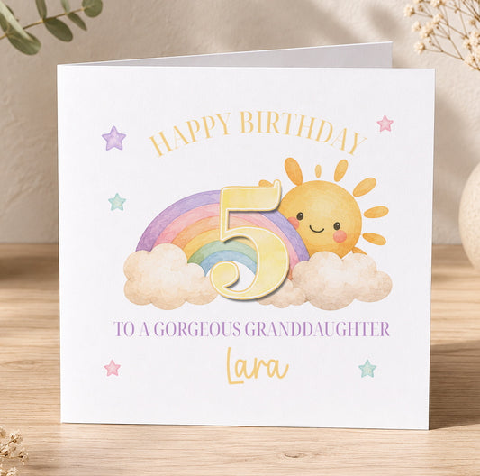 Birthday card featuring a colourful illustration of a sun, clouds and a rainbow, printed with 'Happy Birthday to a Gorgeous Granddaughter Lara'.