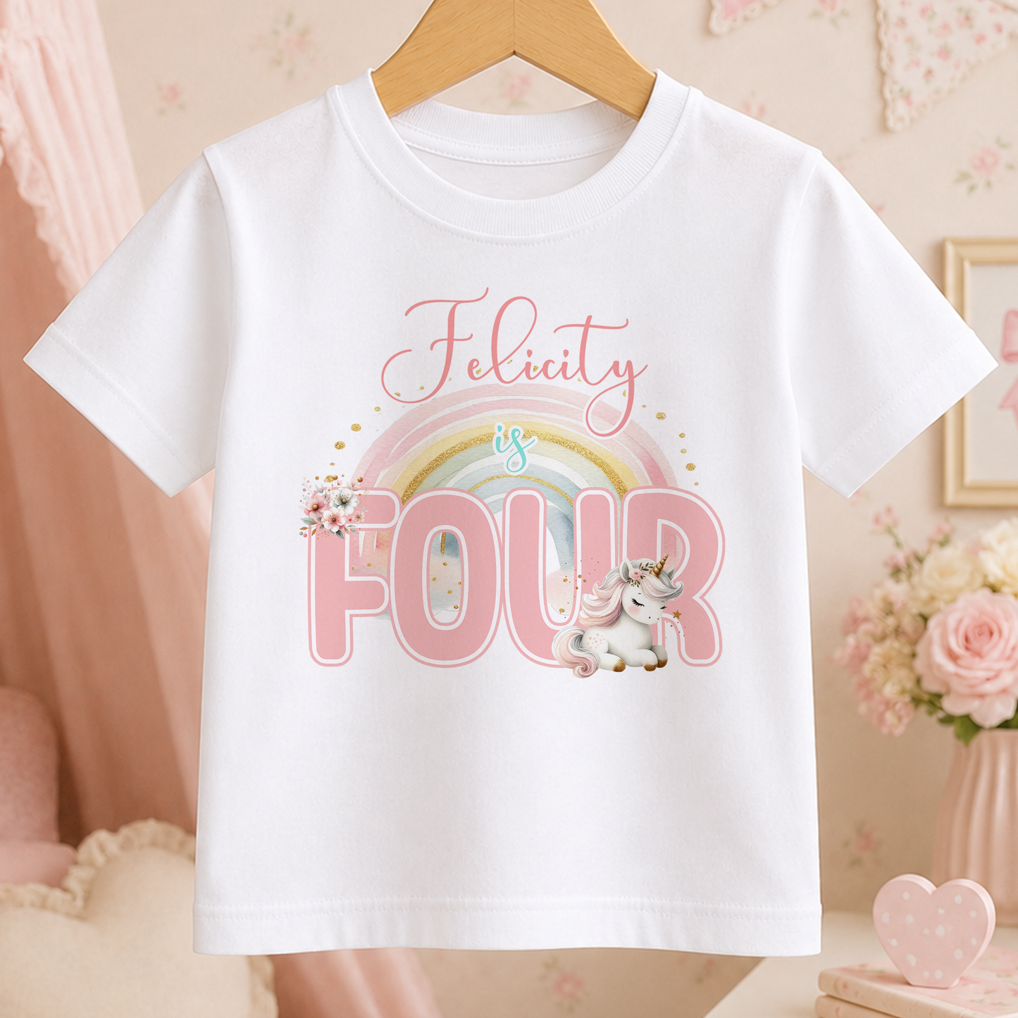 A white t-shirt with a pink unicorn and rainbow graphic, along with the text "Felicity is FOUR" printed on it.