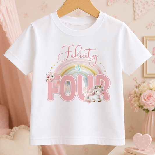A white t-shirt with a pink unicorn and rainbow graphic, along with the text "Felicity is FOUR" printed on it.