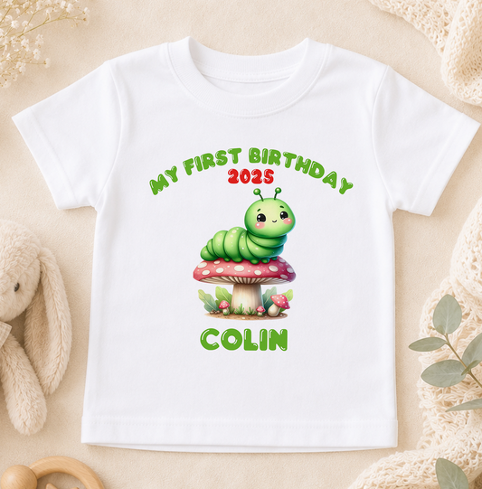 A white t-shirt with a cartoon caterpillar on a mushroom and text that says "My first birthday 2005 COLIN".