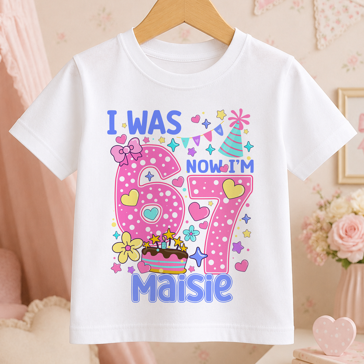 White t-shirt with a pastel 'I Was 6, Now I'm 7' birthday design featuring stars, hearts and a birthday cake.