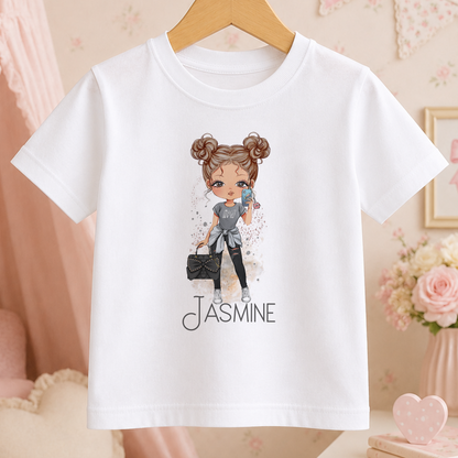 A white t-shirt with a cartoon illustration of a young girl wearing a gray outfit and holding a black purse. The text "JASMINE" is printed below the illustration.