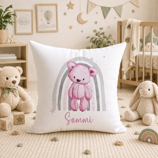 White nursery cushion printed with a pink teddy bear and grey rainbow design, personalised with the name Sammi, styled in a baby's nursery.
