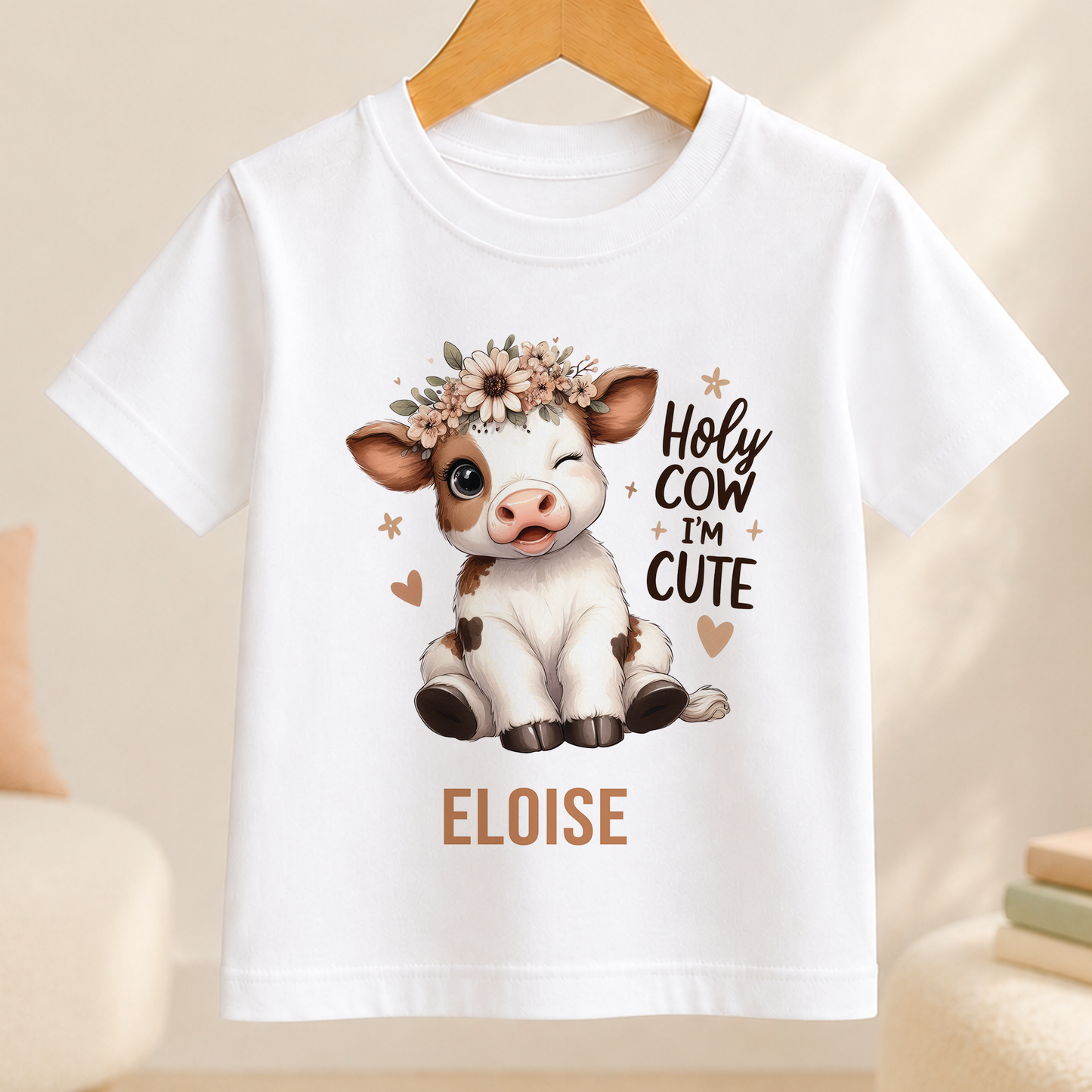 A white t-shirt with a cartoon cow wearing a flower crown and the text "HOLY COW I'M CUTE" printed on it.