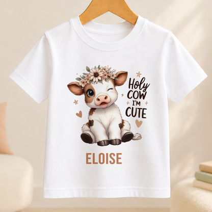 A white t-shirt with a cartoon cow wearing a flower crown and the text "HOLY COW I'M CUTE" printed on it.