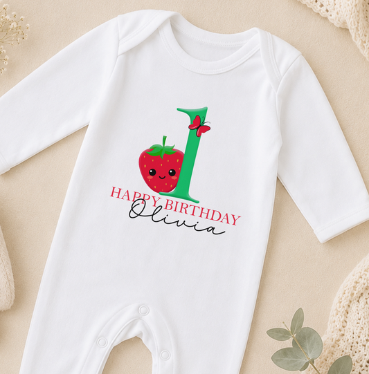 A white onesie with a red strawberry and green number one, along with the text "Happy Birthday Olivia" printed on it.