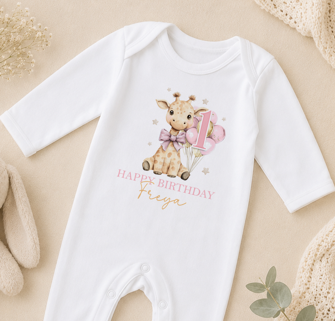 Personalised white baby vest printed with a giraffe and balloons and 'Happy Birthday Freya', styled on a beige backdrop.
