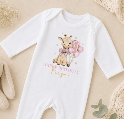 Personalised white baby vest printed with a giraffe and balloons and 'Happy Birthday Freya', styled on a beige backdrop.