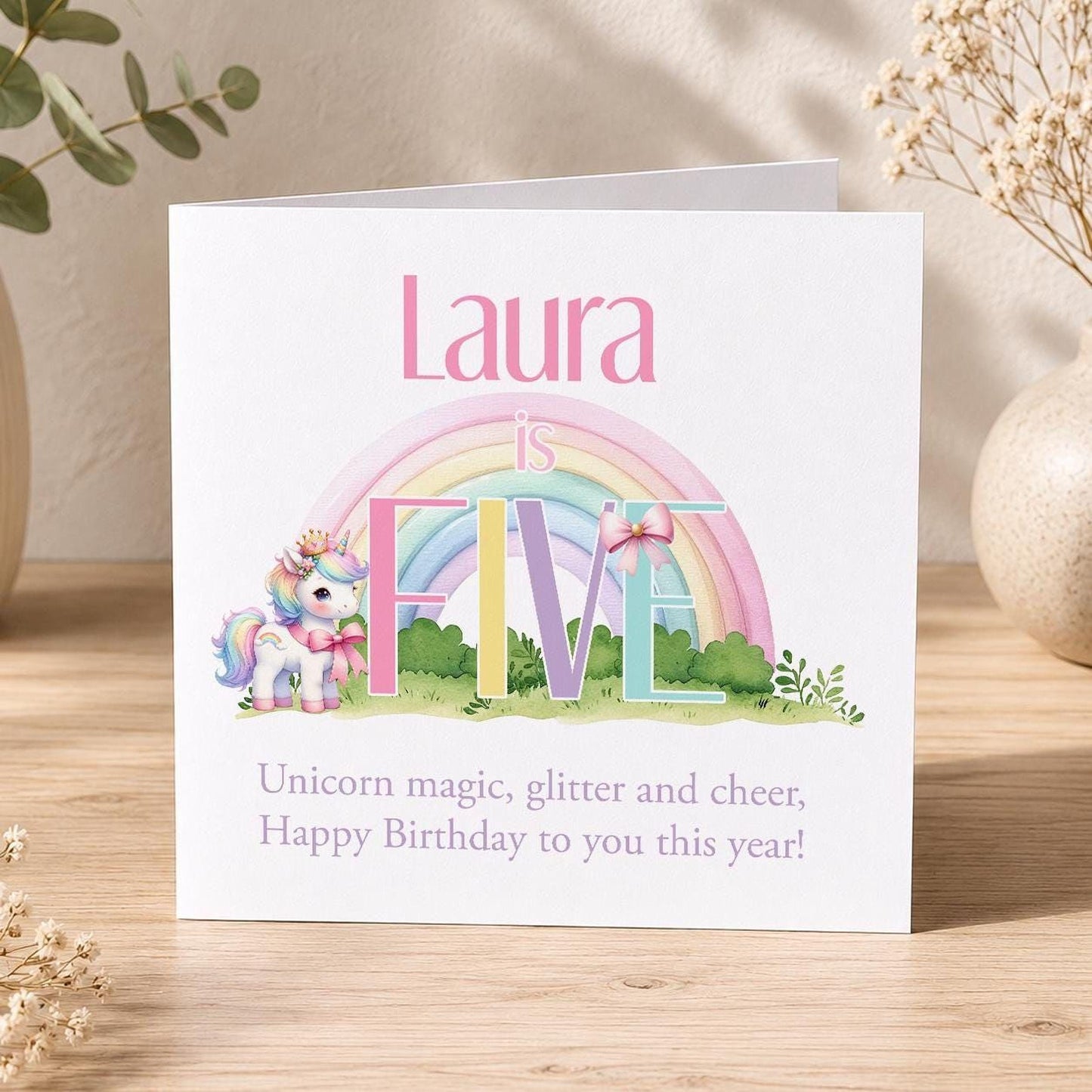 Square birthday card featuring a pastel rainbow and unicorn design, personalised with a girl's name and age.