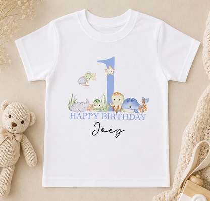 A white t-shirt with a graphic design featuring a blue number 1, surrounded by various sea animals, and the text "Happy Birthday Joey" printed on it.
