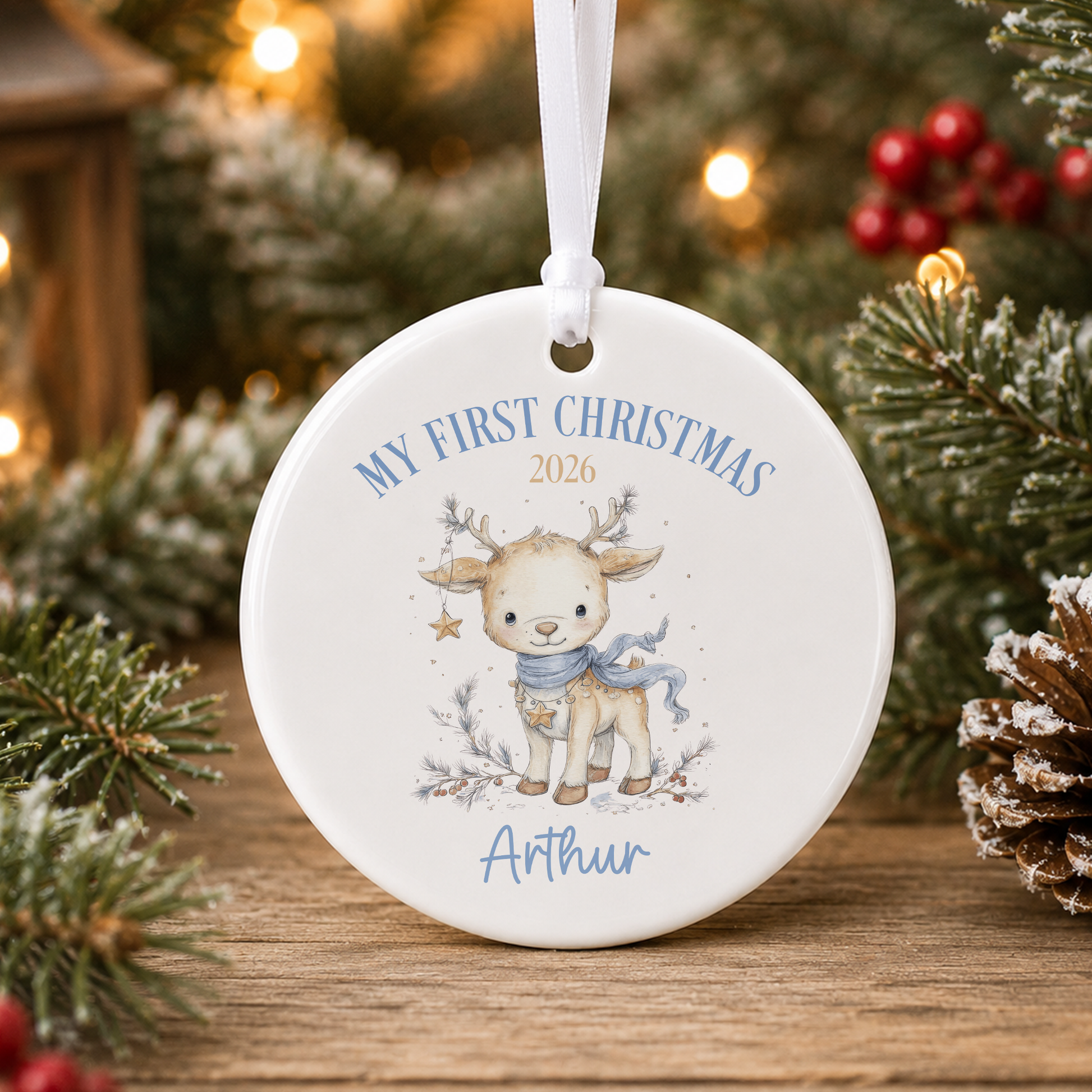 A white ornament with a deer and the text "My first Christmas" and "Athur" printed on it, hanging on a Christmas tree.