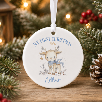 A white ornament with a deer and the text "My first Christmas" and "Athur" printed on it, hanging on a Christmas tree.