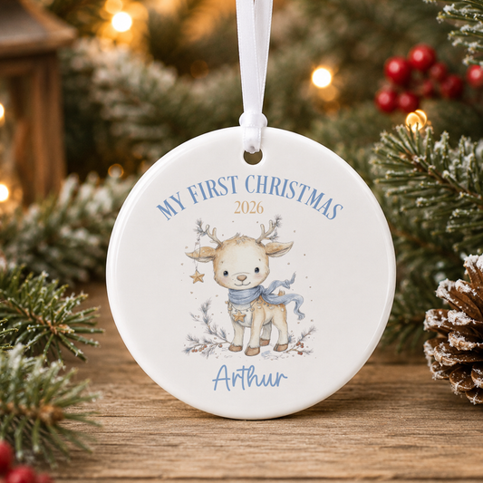 A white ornament with a deer and the text "My first Christmas" and "Athur" printed on it, hanging on a Christmas tree.