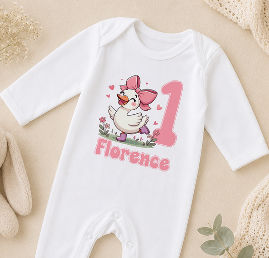 A white onesie with a cartoon duck and the name "Florence" printed on it, along with a pink number 1.