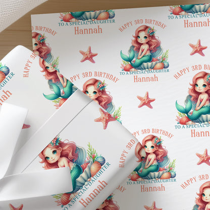 Close-up of personalised mermaid birthday wrapping paper with a repeating pastel mermaid, seashell and starfish pattern on premium white gift wrap.