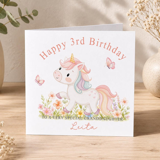 Square personalised birthday card showing a pastel unicorn with rainbow mane among watercolour flowers and pink butterflies, reading Happy 3rd Birthday to a very special Granddaughter.