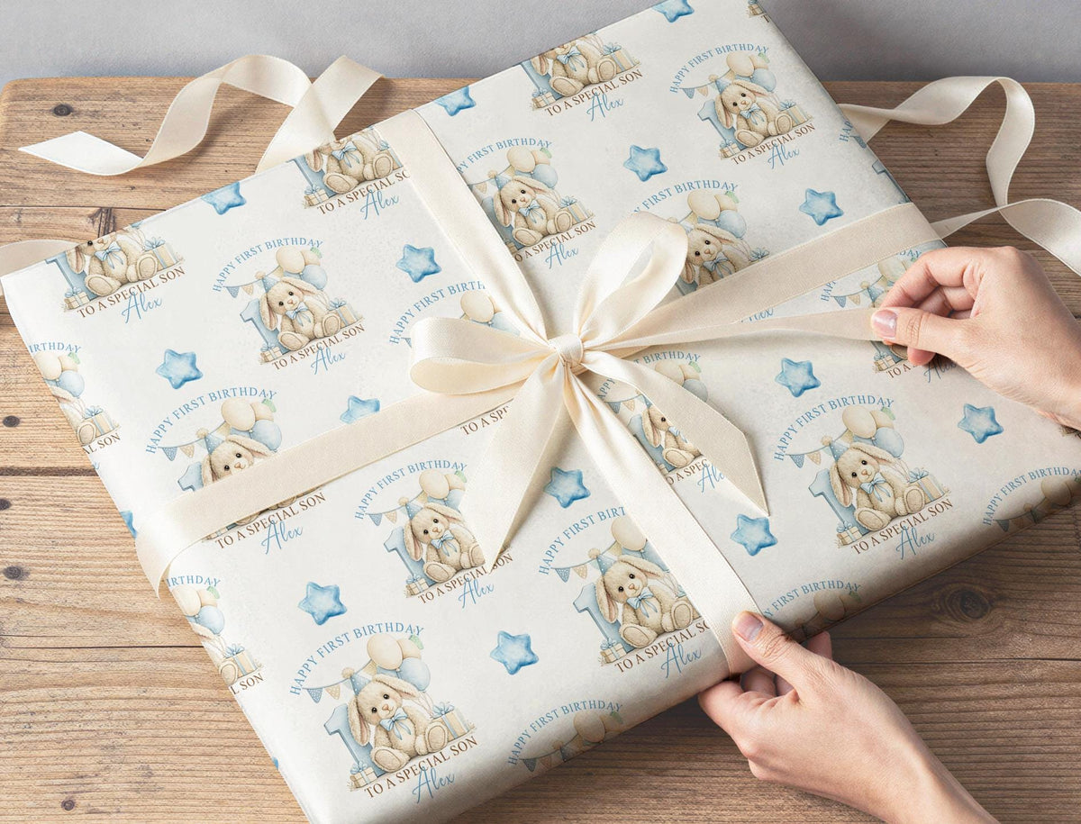 Personalised blue bunny wrapping paper wrapped around a gift with ribbon, featuring the custom name, blue number one and balloons.