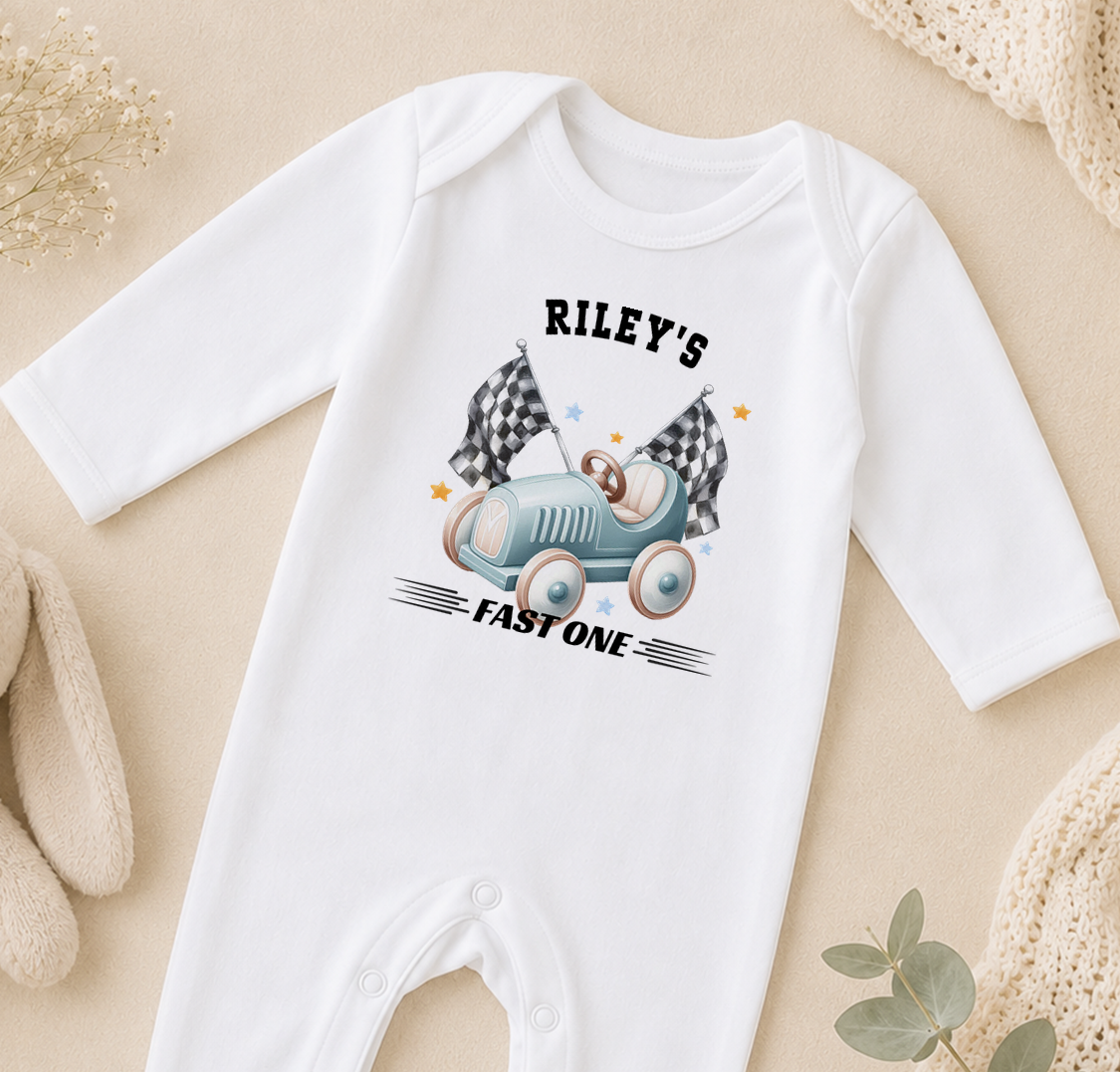 White baby onesie printed with a race car design and the text 'Riley's FAST ONE'.