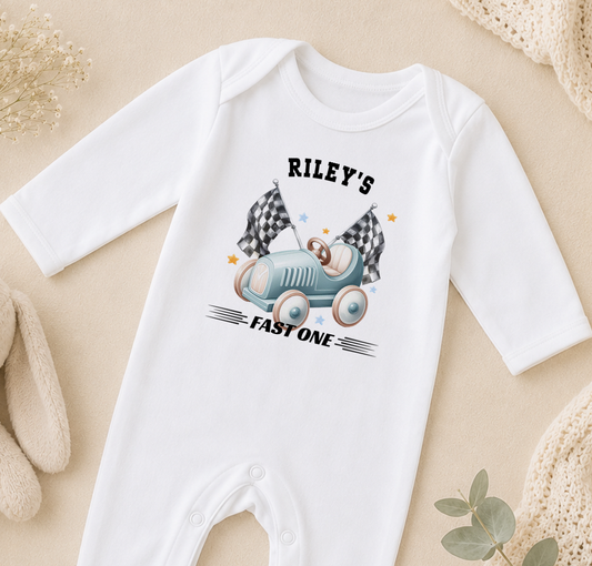 A white onesie with a graphic of a race car and the text "Riley's FAST ONE" printed on it.