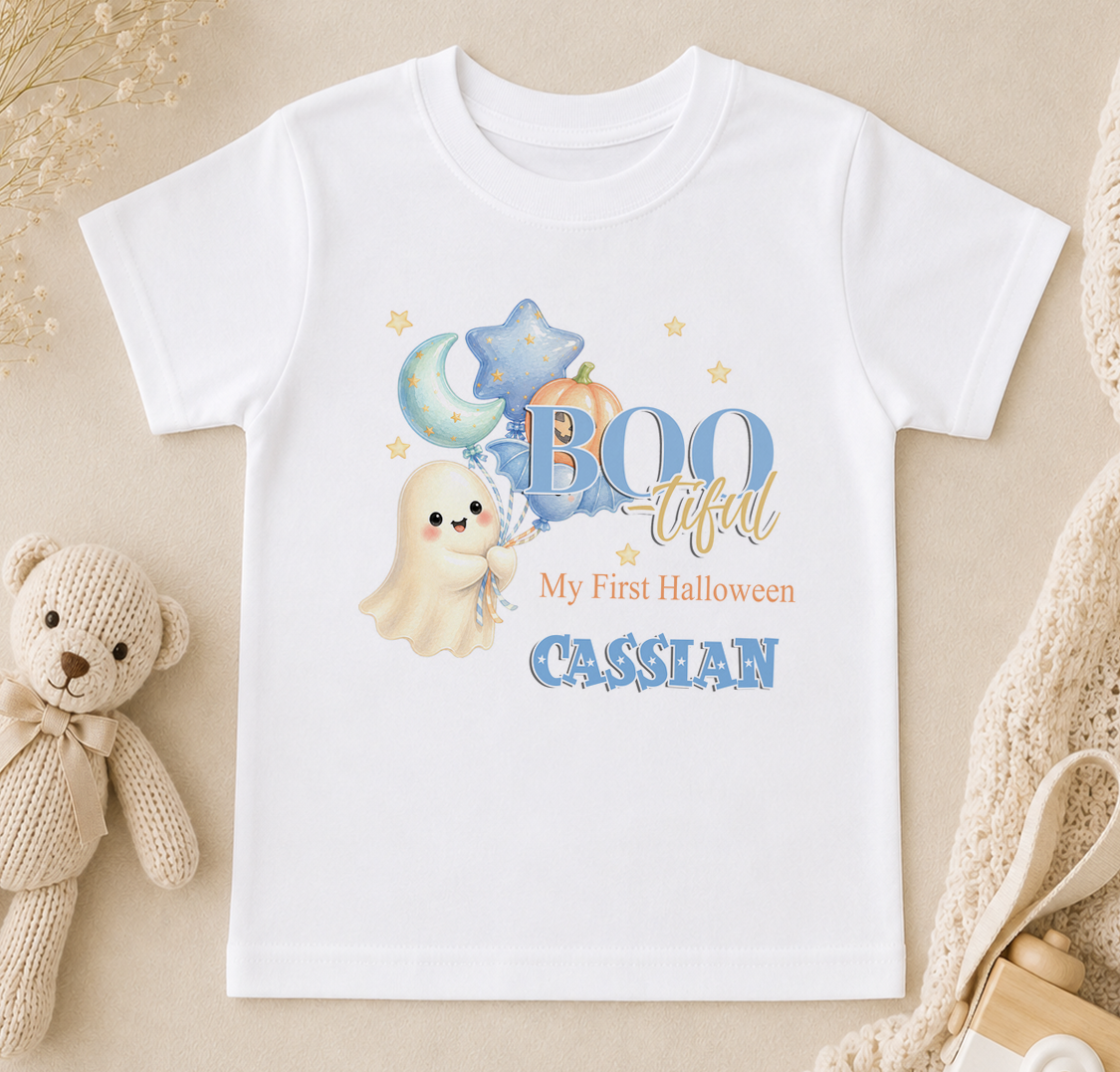 A white t-shirt with a Halloween-themed design, including a ghost, pumpkin, and stars, along with the text "My First Halloween" and "CASSIAN".