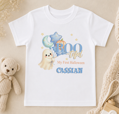 A white t-shirt with a Halloween-themed design, including a ghost, pumpkin, and stars, along with the text "My First Halloween" and "CASSIAN".
