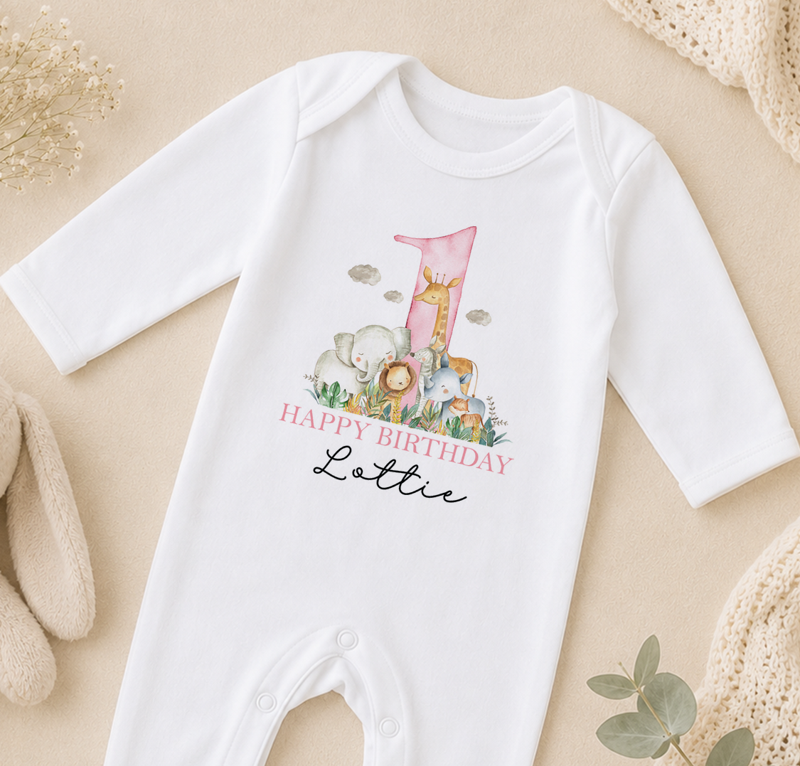 A white onesie with a printed design of animals and the text "Happy Birthday Lottie" on it, placed on a beige surface.