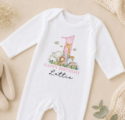 A white onesie with a printed design of animals and the text "Happy Birthday Lottie" on it, placed on a beige surface.