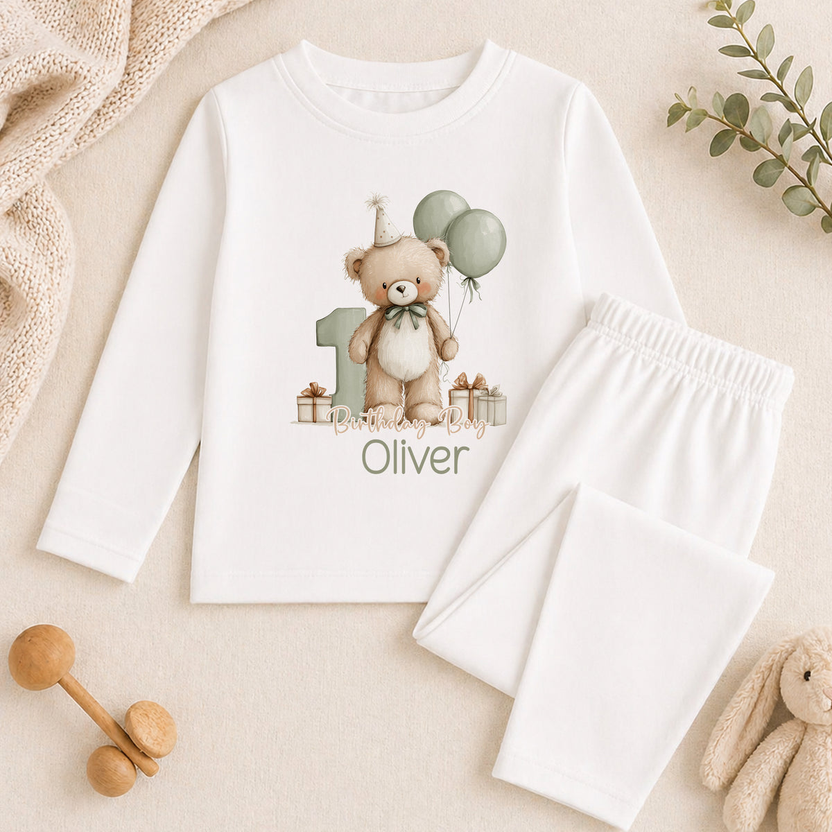 A white long-sleeved shirt with a teddy bear and balloons printed on it, along with a pair of white pants and some stuffed animals.