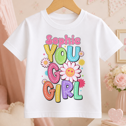 A white t-shirt with a colorful graphic design featuring the text "Sophie You Go Girl" surrounded by flowers and other decorative elements.
