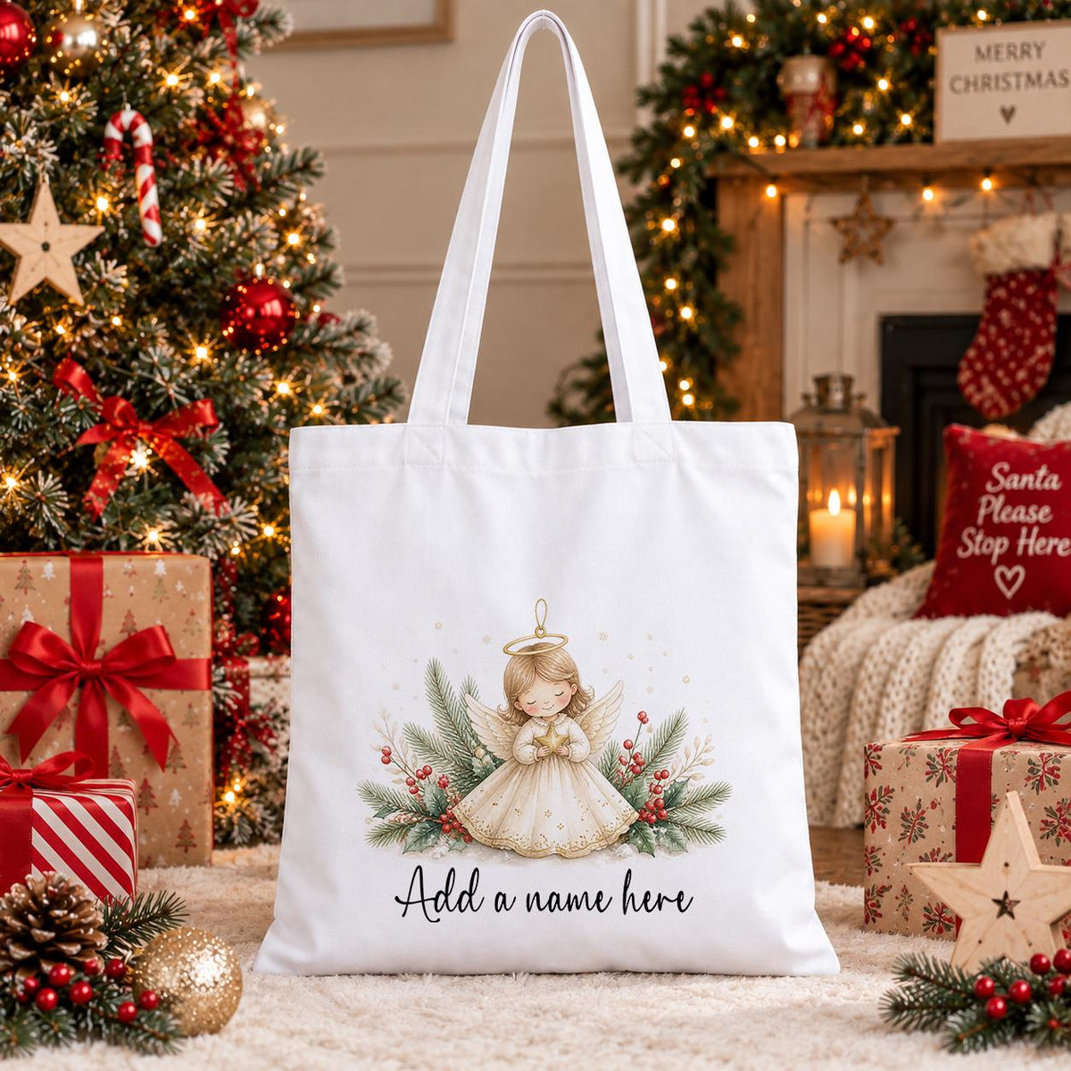 White cotton tote bag printed with a watercolour angel with a gold halo and wings, pine branches and red berries, above a name in script.