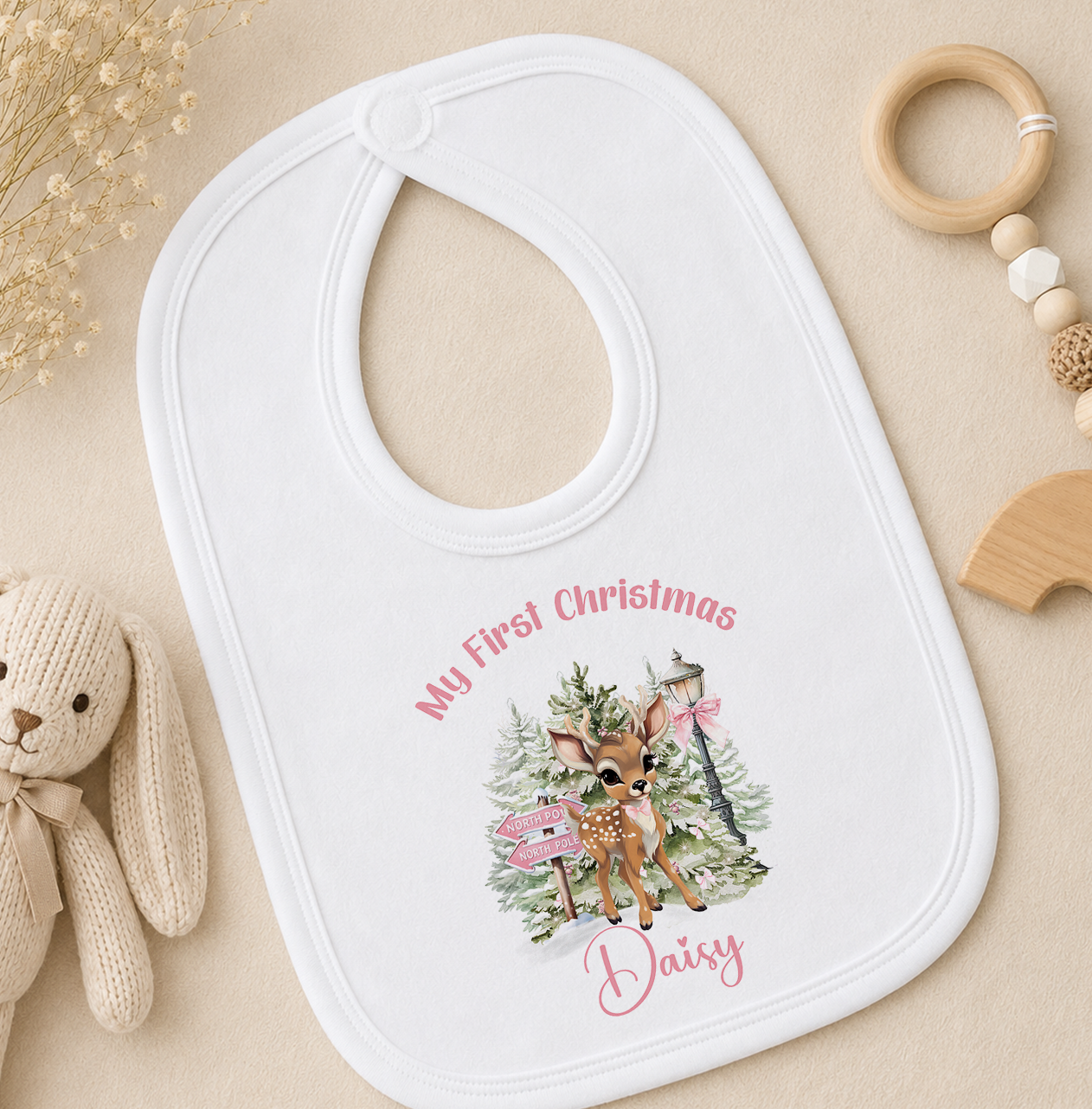 A white baby bib with a personalized design featuring a deer and Christmas trees, along with the text "My First Christmas Daisy".