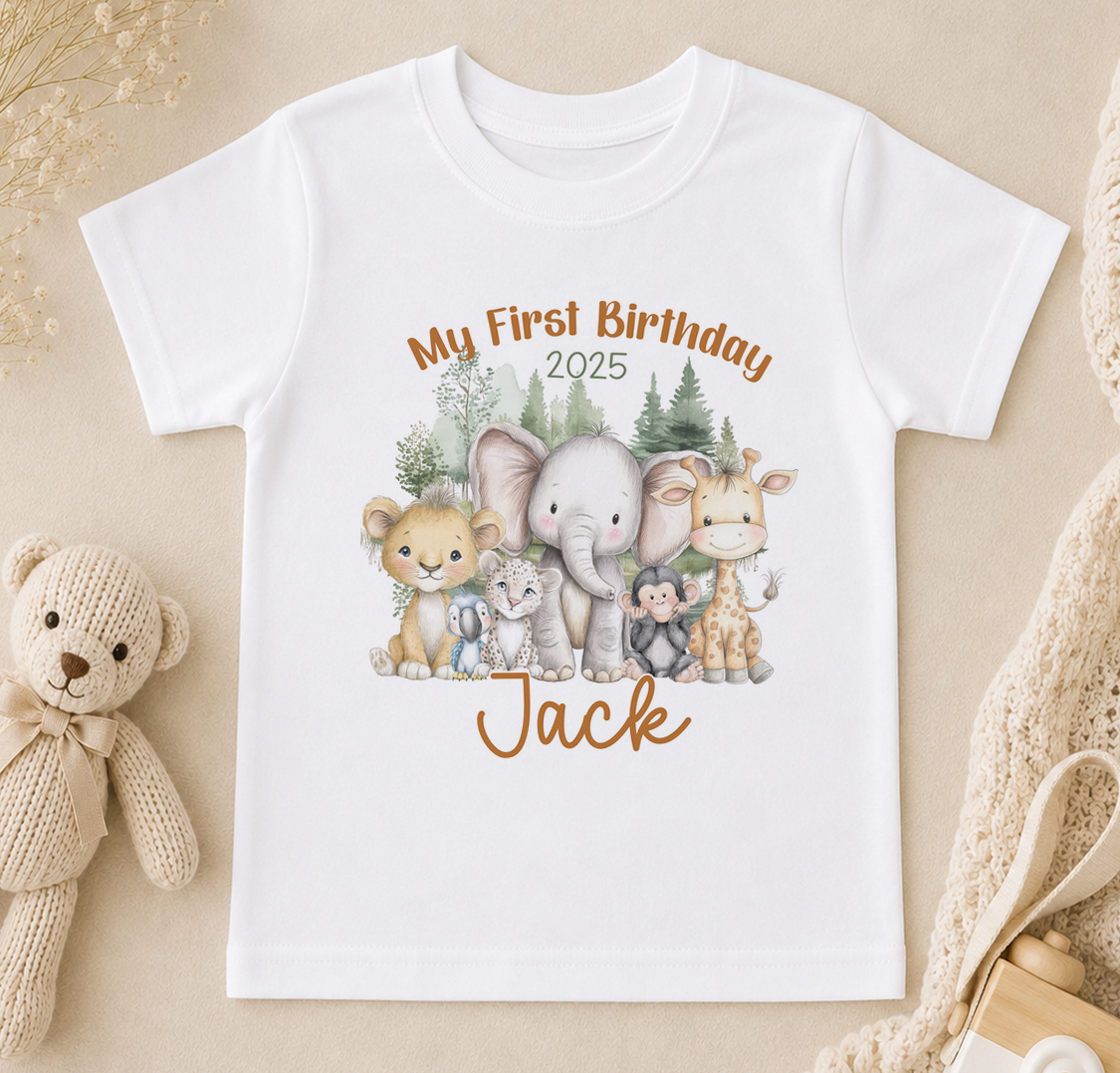 A white t-shirt with a printed design of various animals, including a lion, elephant, giraffe, and teddy bear, along with the text "My First Birthday Jack" and the year "2025".