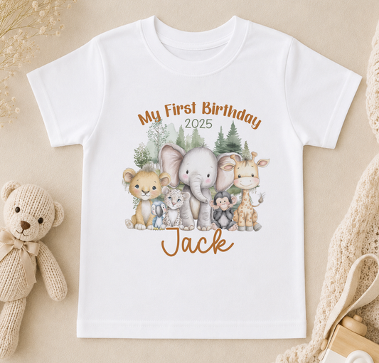 A white t-shirt with a printed design of various animals, including a lion, elephant, giraffe, and teddy bear, along with the text "My First Birthday Jack" and the year "2025".