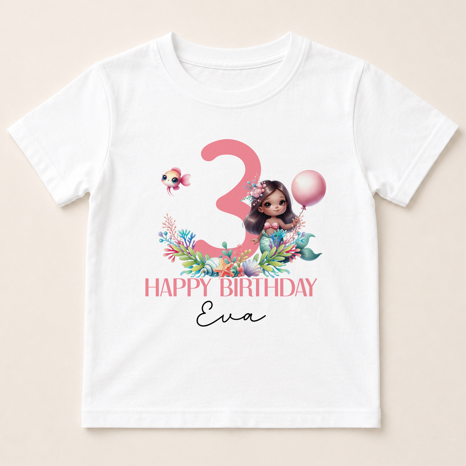 A white t-shirt with a graphic design featuring a mermaid character, a number 3, and a balloon. The text below the design reads "Happy Birthday Eva".
