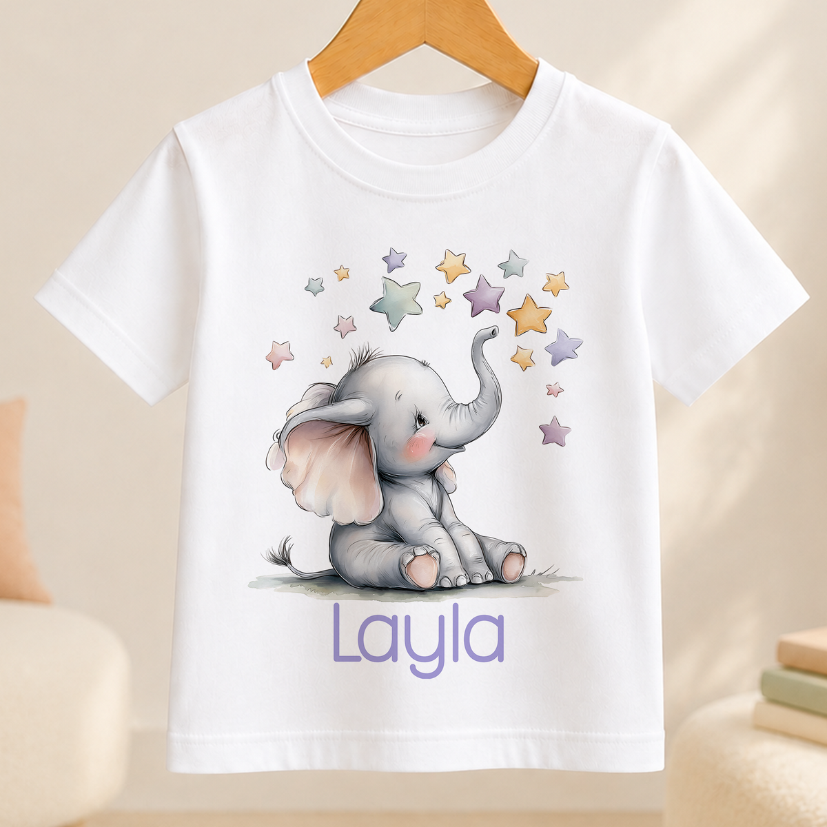 A white t-shirt with a drawing of a baby elephant surrounded by stars and the name "Layla" written below it.