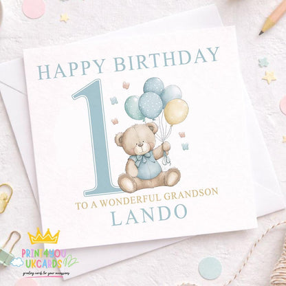 Square birthday card with a teddy bear holding pastel balloons beside a large number 1, personalised To a Wonderful Grandson Lando, resting on an envelope.