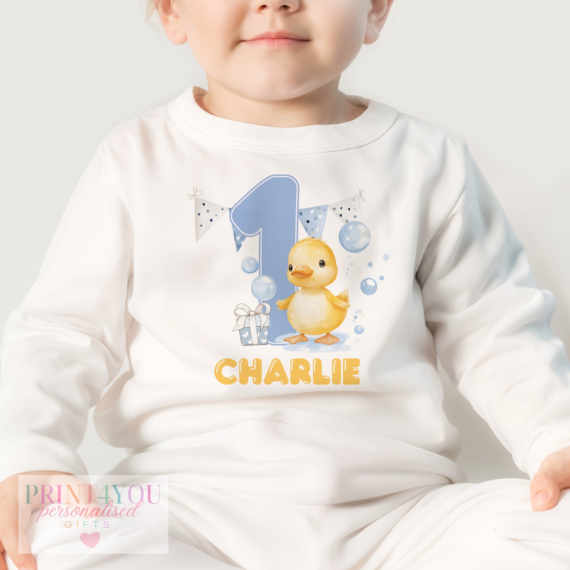 Close-up of the yellow duck and bubbles design personalised with baby's name on first birthday pyjamas.