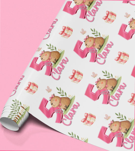 Roll of personalised pink birthday wrapping paper featuring a repeating capybara design wearing a party hat and holding a gift.