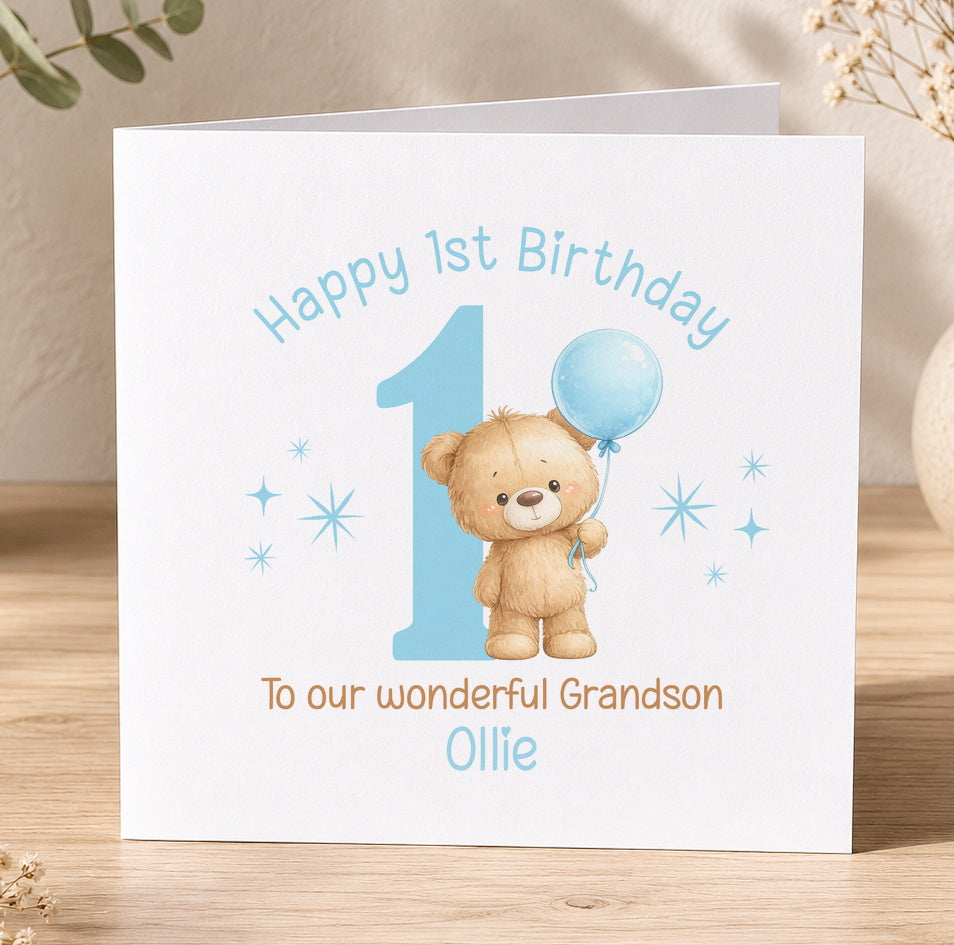 White greeting card illustrated with a teddy bear holding a blue balloon, celebrating a first birthday, personalised with the boy's name.