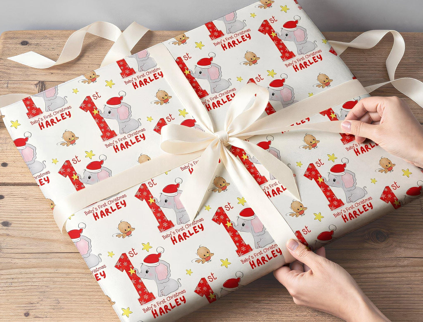 Hands wrapping a gift in personalised Baby's First Christmas elephant wrapping paper with a white ribbon.