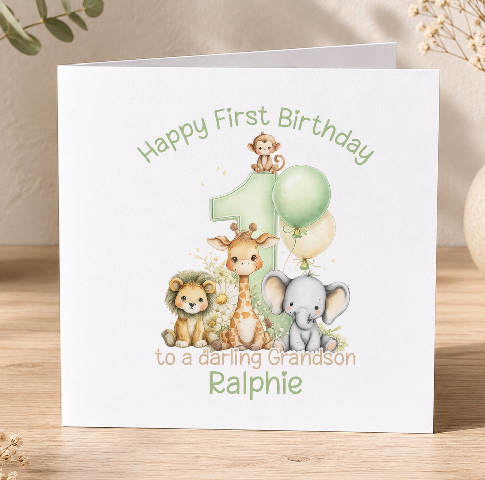 Personalised first birthday card featuring a cartoon lion, giraffe and elephant beside a green number 1, reading Happy First Birthday to a lovely Grandson Ralphie.