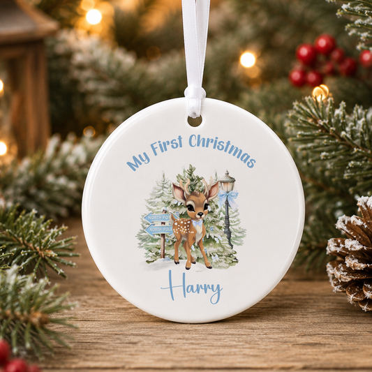 A white oval ornament with a deer and Christmas trees, hanging on a string.